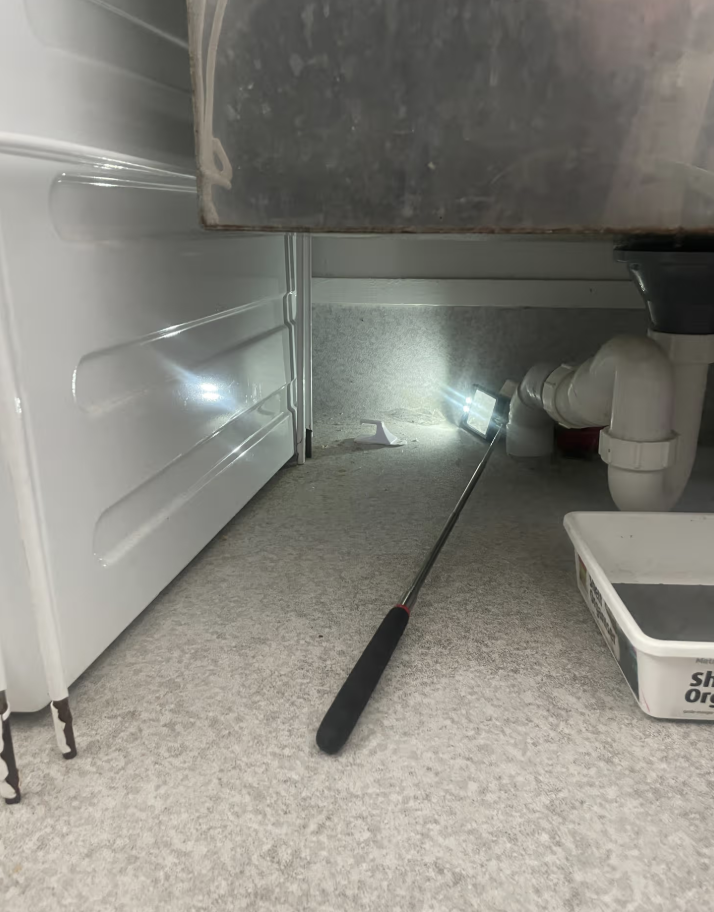 Torchlit check of the space beneath a kitchen unit, an internal station in place